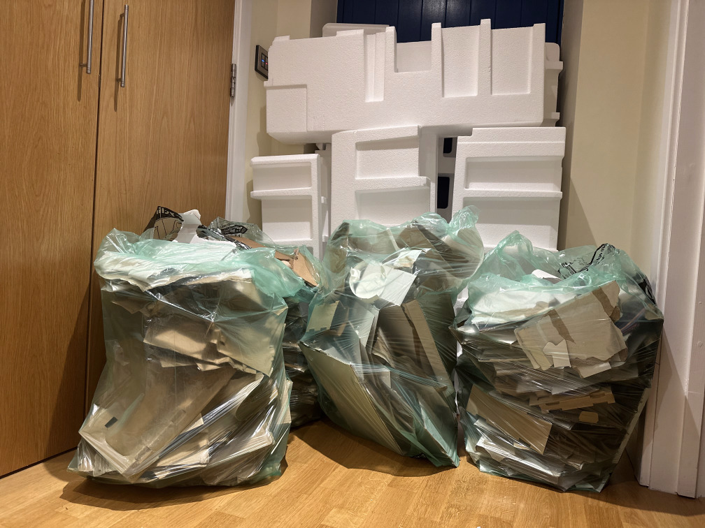 Four recycling bags filled with cut-up cardboard packaging, with lots of polystyrene in the background