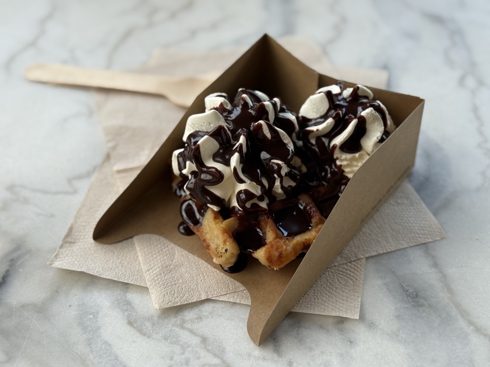 A waffle with whipped cream and chocolate sauce
